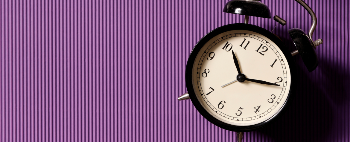 Photograph of a table clock on a purple background.