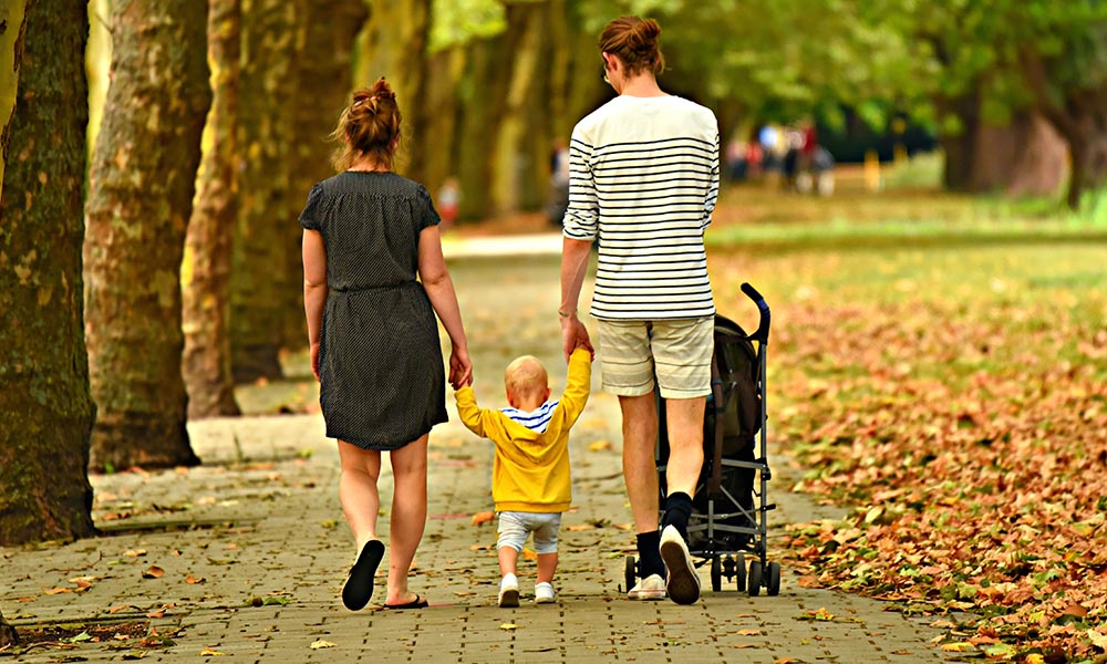 Parents walking a toddler and baby in the park.