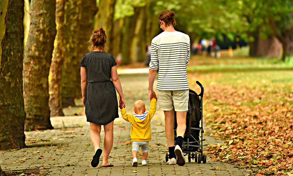 Parents walking a toddler and baby in the park.