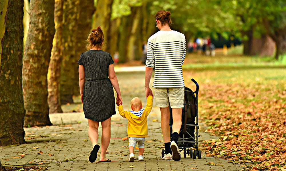 Parents walking a toddler and baby in the park.